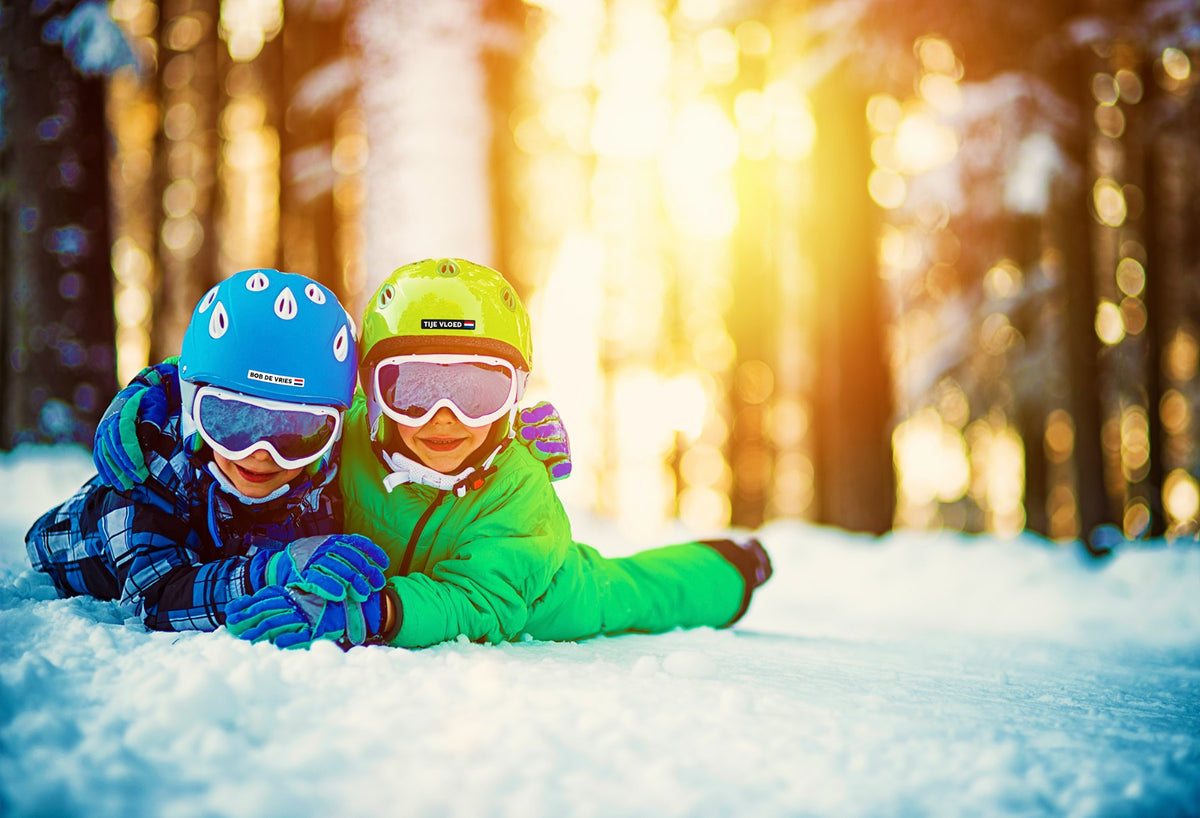 Due bambini sulla neve con un adesivo con nome sul casco da sci