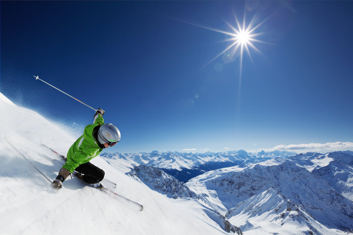 Skier with a green name sticker on his helmet skiing down in the sun, with mountains in the background