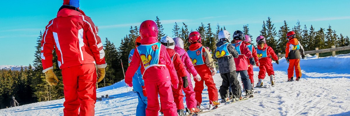 Ski school group of children in a line behind their ski instructor on the slope